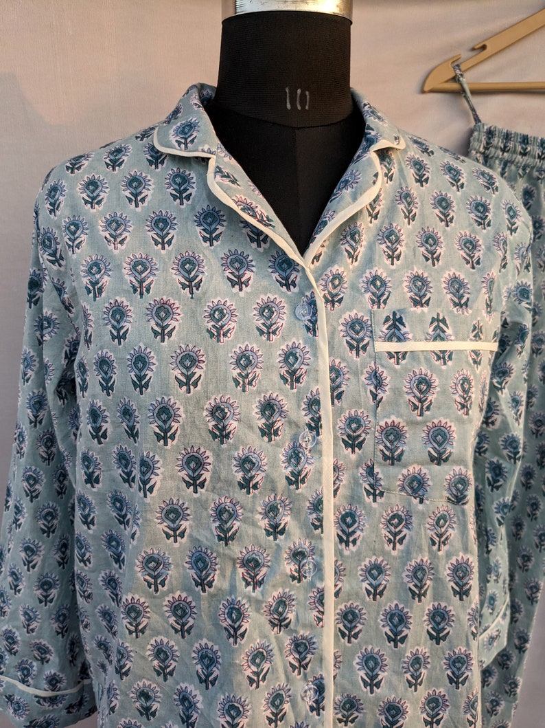 May include: A light blue pajama top with a white trim and a floral print. The top has a button-up front and long sleeves.