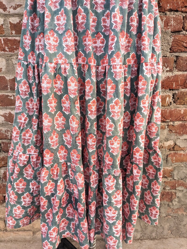 May include: A tiered maxi skirt with a floral print in shades of green, pink, and white. The skirt has a relaxed fit and a flowy silhouette.
