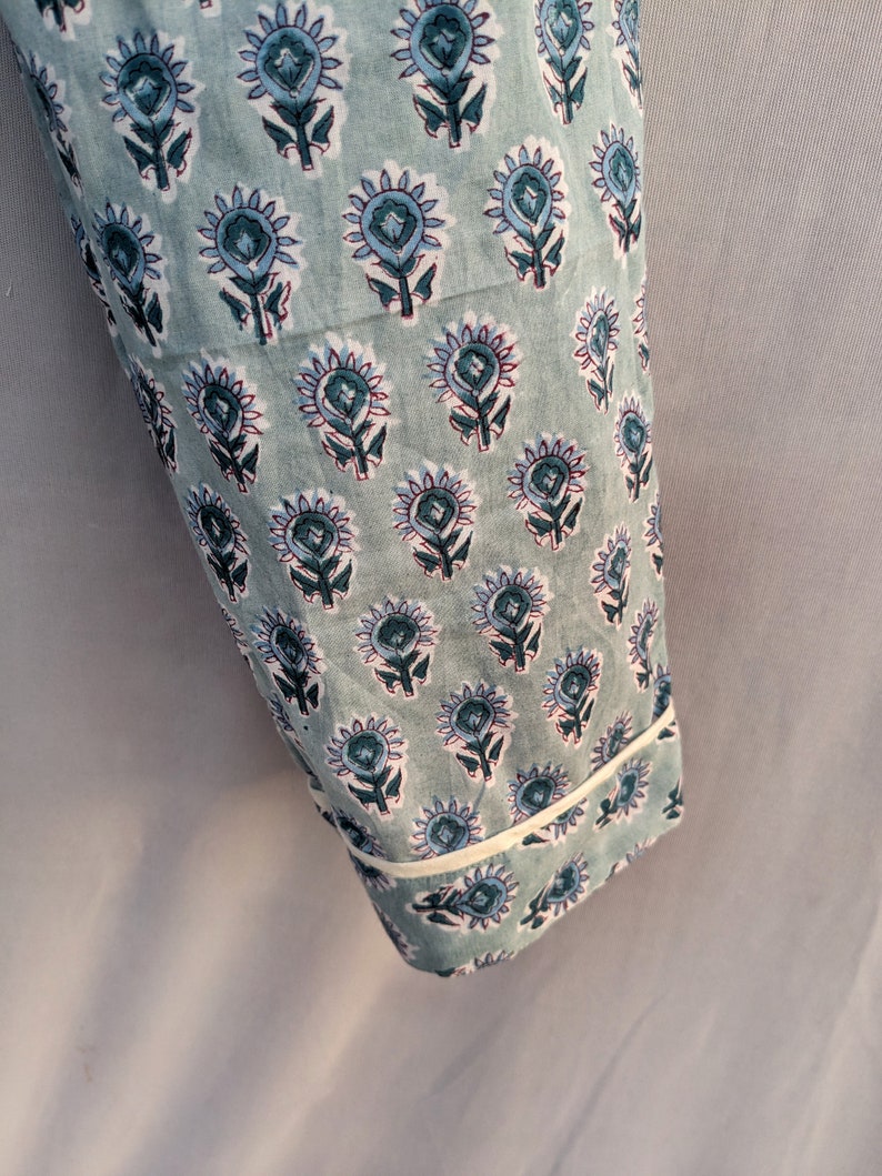 May include: A close-up of a light blue fabric with a white trim. The fabric has a repeating pattern of blue and green floral designs.