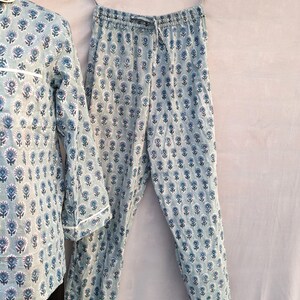 May include: A blue and white floral print pajama set with long sleeves and pants. The pajamas have a drawstring waistband and a white trim.