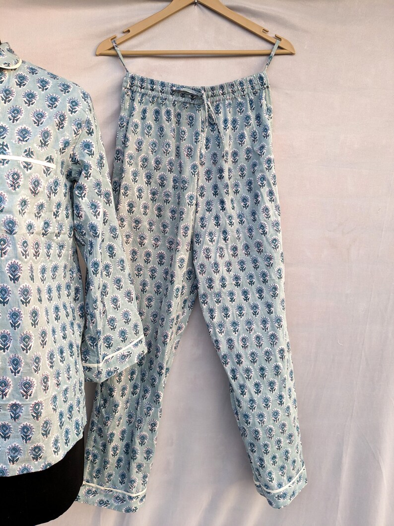 May include: A blue and white floral print pajama set with long sleeves and pants. The pajamas have a drawstring waistband and a white trim.