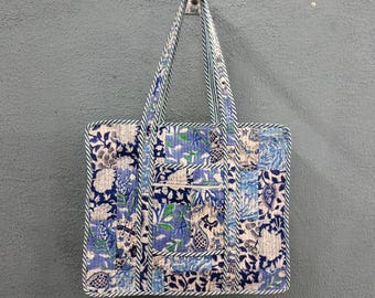 May include: A blue and white patchwork tote bag with a floral print. The bag has a single handle and is hanging on a hook.