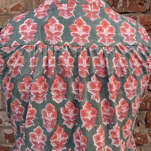 May include: A sleeveless green cotton top with a pink floral print. The top has a button-up collar and a gathered waist.