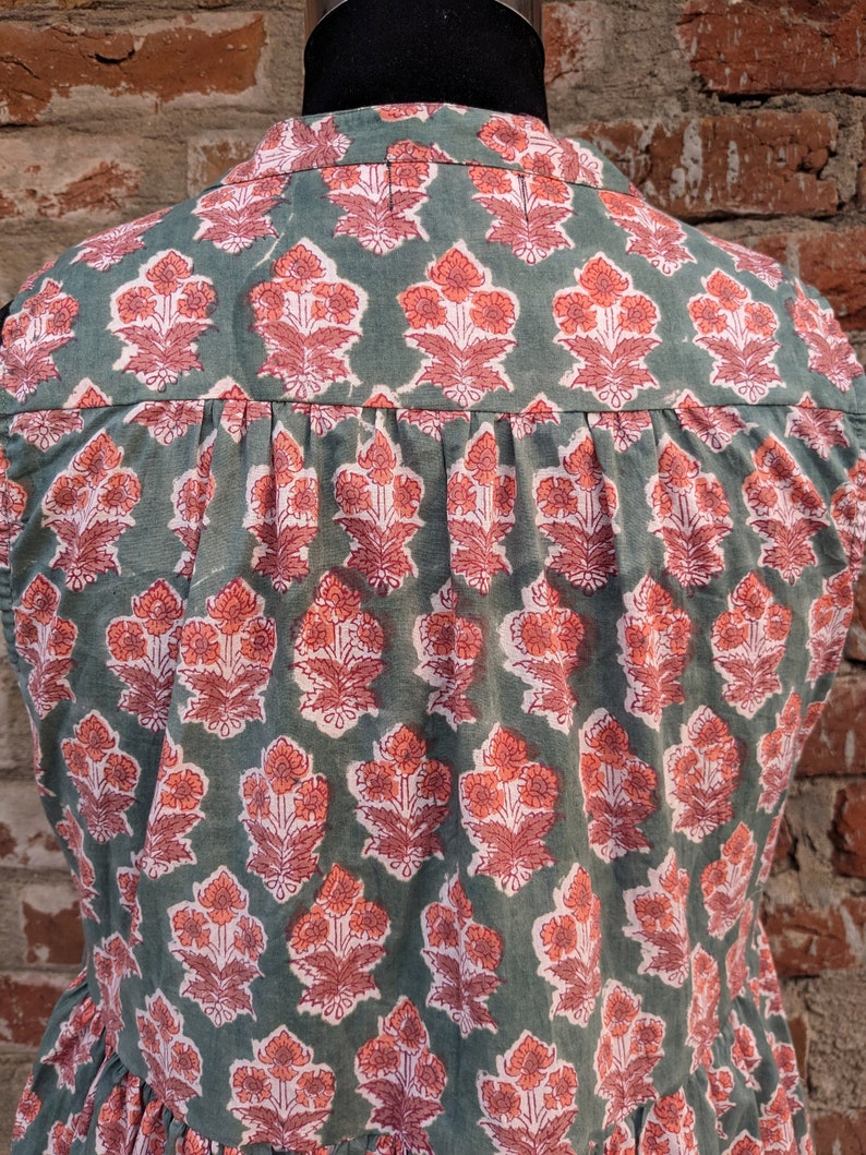 May include: A sleeveless green cotton top with a pink floral print. The top has a button-up collar and a gathered waist.