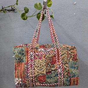 Puede incluir: Una bolsa de mano estilo patchwork con asas de rayas rojas, blancas y azules. La bolsa está hecha de una tela acolchada con un patrón floral.