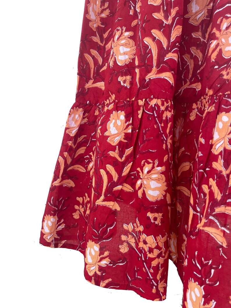 May include: A section of a red fabric with a floral pattern. The design features large, stylized flowers in shades of peach and white, set against a deep red background. The fabric has a tiered, ruffled edge.
