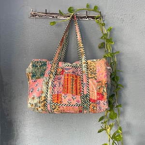 May include: A patchwork style tote bag with a pink, orange, green and white floral print. The bag has a green and white striped trim and is hanging on a hook.