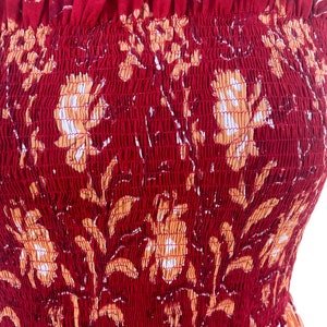 May include: A red sundress with a floral pattern in shades of orange and white. The dress features a smocked bodice and thin straps. The fabric has a textured appearance.