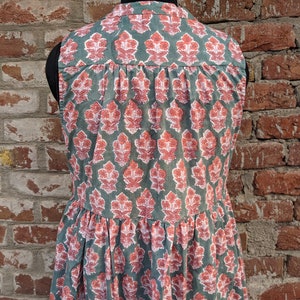 May include: A sleeveless dress with a green background and a pink floral pattern. The dress has a tiered skirt and a round neckline.
