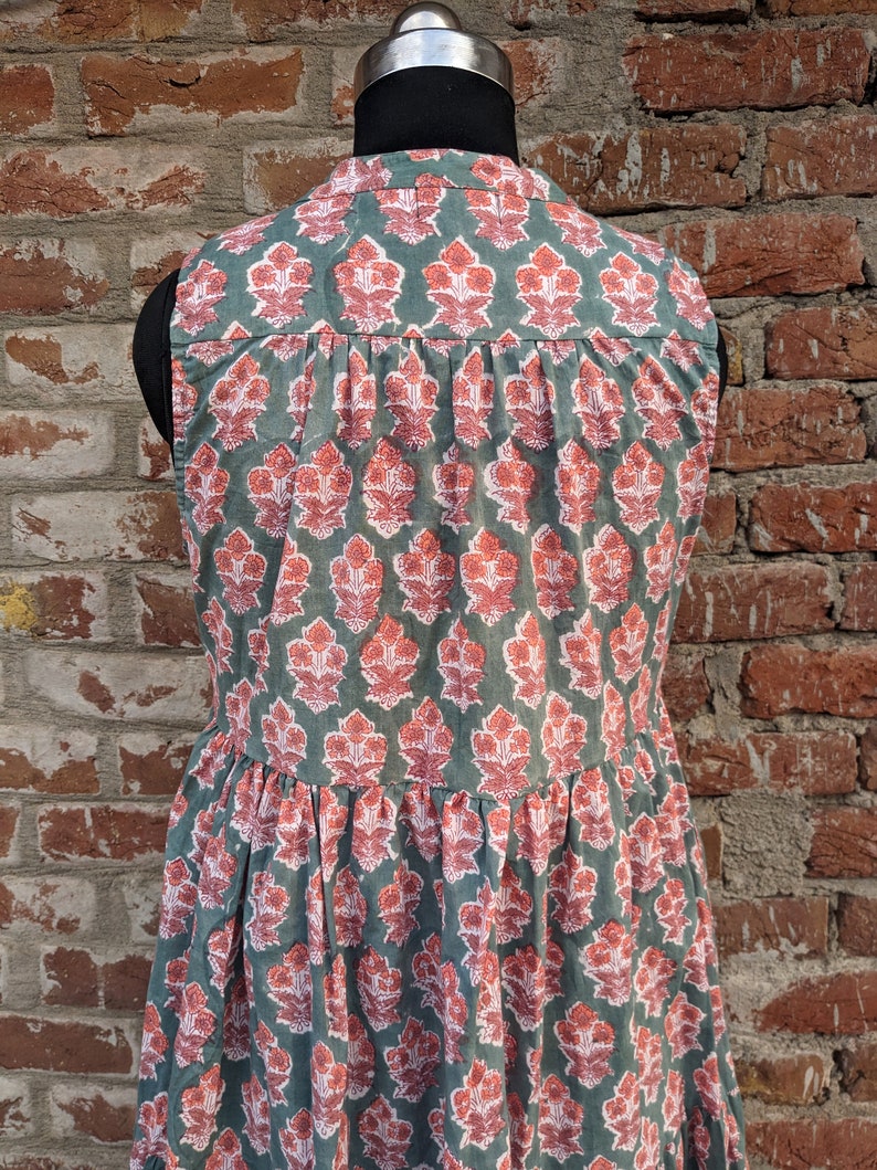 May include: A sleeveless dress with a green background and a pink floral pattern. The dress has a tiered skirt and a round neckline.