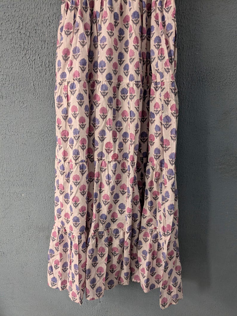 May include: A white tiered maxi dress with a pink and blue floral print. The dress has a fitted bodice and a flowy skirt.