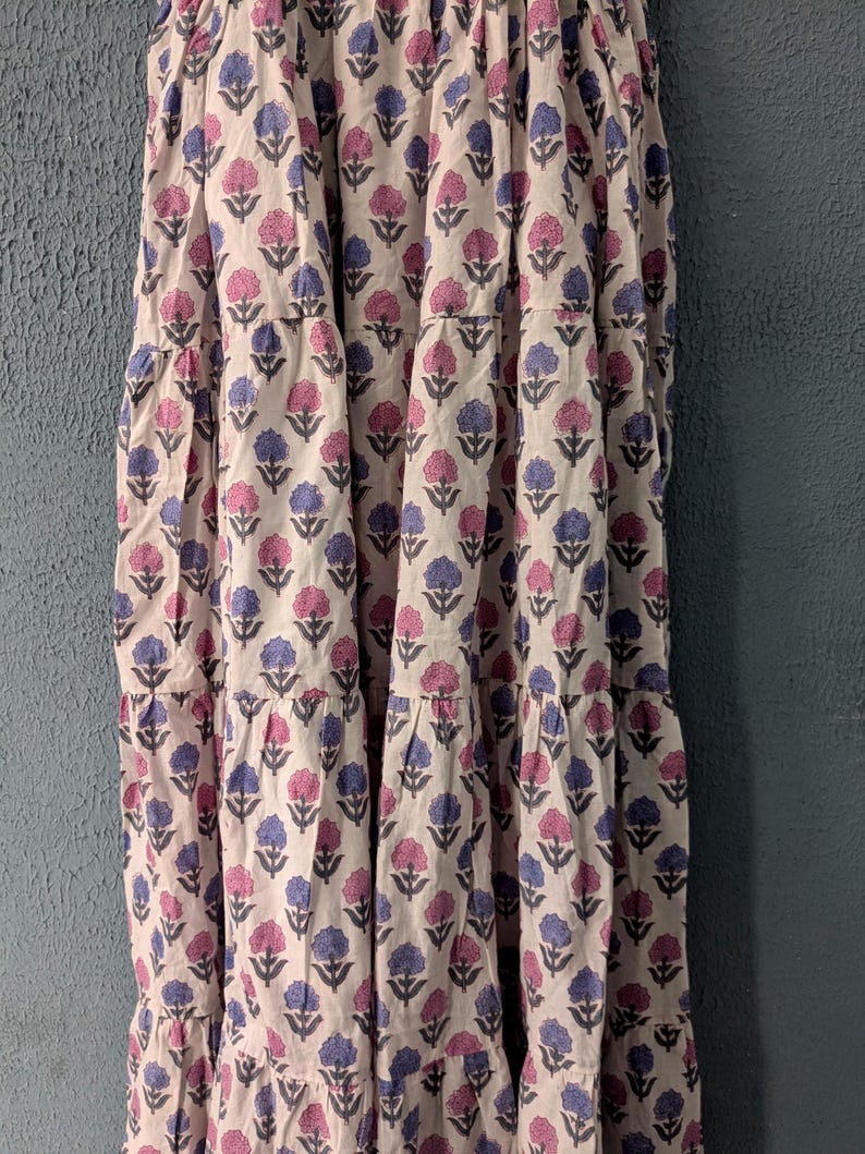 May include: A white maxi skirt with a floral print in shades of pink and blue. The skirt has multiple tiers and a flowy silhouette.