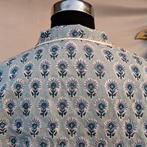 May include: A light blue shirt with a white and blue floral pattern. The shirt has a collar and a button-up front.