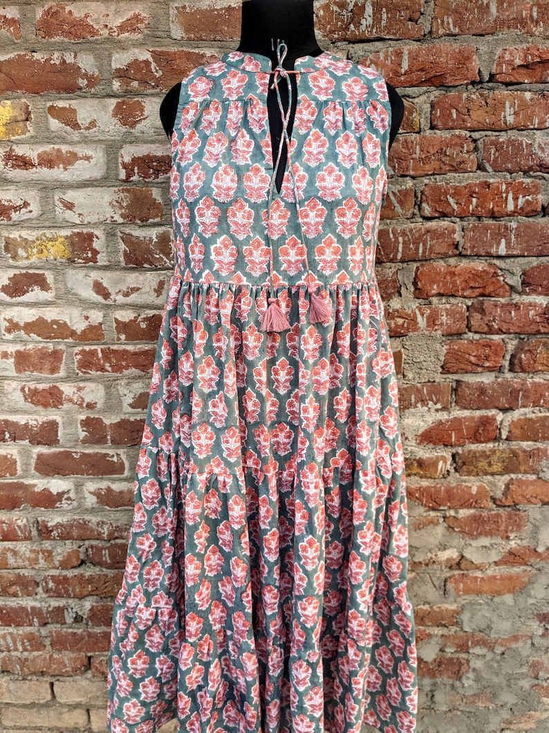 May include: A sleeveless, tiered maxi dress with a floral print in shades of pink and green. The dress has a tie at the neckline and a tassel detail.