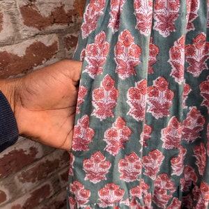 May include: A green cotton dress with a floral print in shades of pink and white. The dress has a gathered skirt and a pocket on the side.