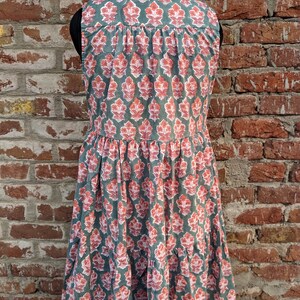 May include: A sleeveless, tiered dress with a green background and a pink floral pattern. The dress has a button-up collar and a relaxed fit.