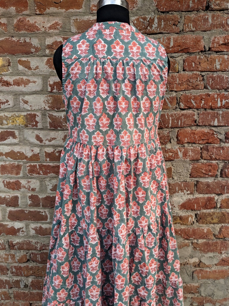May include: A sleeveless, tiered dress with a green background and a pink floral pattern. The dress has a button-up collar and a relaxed fit.