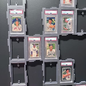 May include: A collection of 1952 Bowman baseball cards, each encased in a protective PSA graded plastic slab. The cards are mounted within a modular gray plastic display frame system, featuring several empty slots for additional card storage.