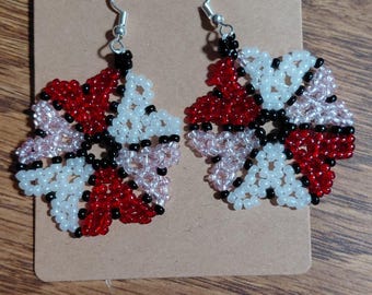 May include: Handmade beaded earrings in a floral design. The earrings feature a flower shape with red, white, pink, and black beads. The earrings are displayed on a brown card against a wooden background.