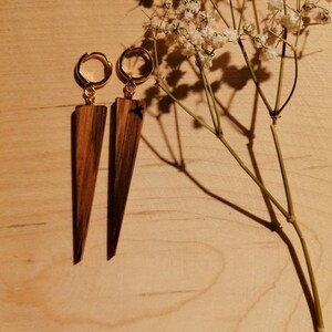 May include: A pair of wooden earrings with gold hoops. The earrings are shaped like a triangle and have a dark wood grain.