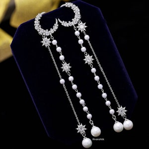 May include: A pair of silver earrings with a crescent moon design, pearl drops, and star accents.