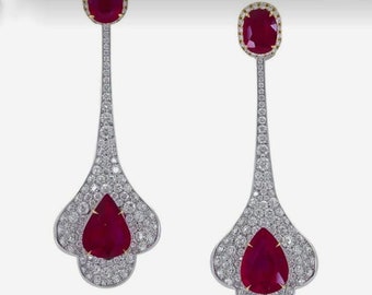 Puede incluir: Un par de pendientes colgantes con una piedra preciosa de rubí rojo y un engaste engastado con diamantes. Los pendientes son de oro blanco y tienen forma de lágrima.