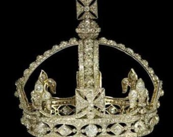 May include: A silver crown with a cross on top and a large diamond in the center. The crown is decorated with smaller diamonds and is set on a black background.