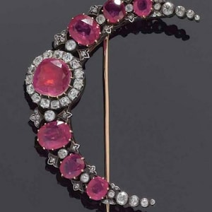 Puede incluir: Un broche en forma de media luna con un engaste de plata y rubíes rojos y diamantes.