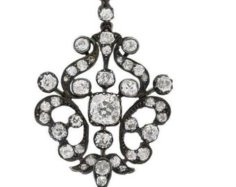 May include: A silver pendant with a delicate, ornate design featuring a central diamond and smaller diamonds surrounding it. The pendant is suspended from a chain with a small diamond at the top.