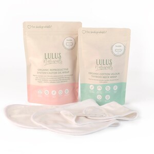 May include: Two pouches of Lulus Naturals organic wraps, one pink and one green, with the text "Organic Reproductive System Castor Oil Wrap" and "Organic Cotton Velour Thyroid Neck Wrap." Several off-white wraps are in front.