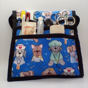 Peut inclure: Un sac médical en toile bleu avec une bordure noire et un imprimé de chien. Le sac a plusieurs poches et est rempli de fournitures médicales, y compris des ciseaux, des stylos et une bouteille de désinfectant pour les mains. Le sac porte l'inscription "LOVE".
