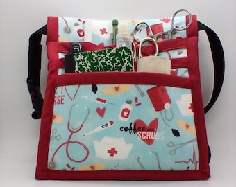 May include: Red and blue patterned fabric waist bag with multiple pockets and a black strap. The bag is filled with medical supplies, including scissors, a pen, and a small notebook. The bag has the text "coffee scrubs" printed on it.