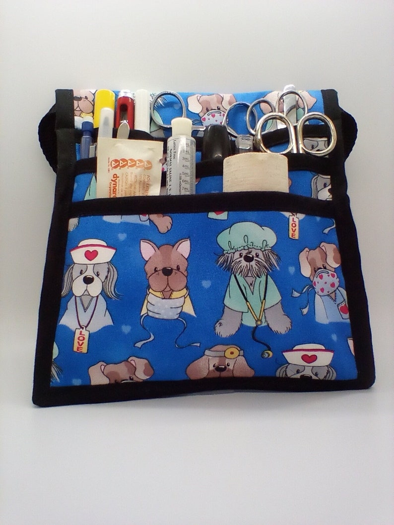Pu&ograve; includere: Una borsa medica in tela blu con bordatura nera e stampa di cani. La borsa ha pi&ugrave; tasche ed &egrave; piena di forniture mediche, tra cui forbici, penne e una bottiglia di disinfettante per le mani. La borsa ha la scritta "LOVE" stampata.