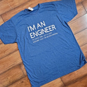 Op de afbeelding: Een blauw T-shirt met witte tekst die luidt: "Ik ben een ingenieur om tijd te besparen, laten we gewoon aannemen dat ik nooit fout zit."