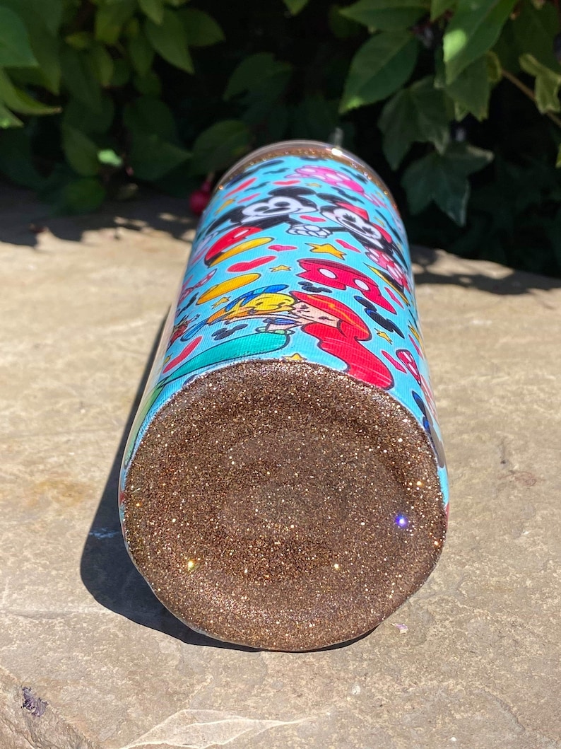 May include: A blue and white tumbler with a glitter bottom. The tumbler features a cartoon design of Mickey Mouse and Minnie Mouse.