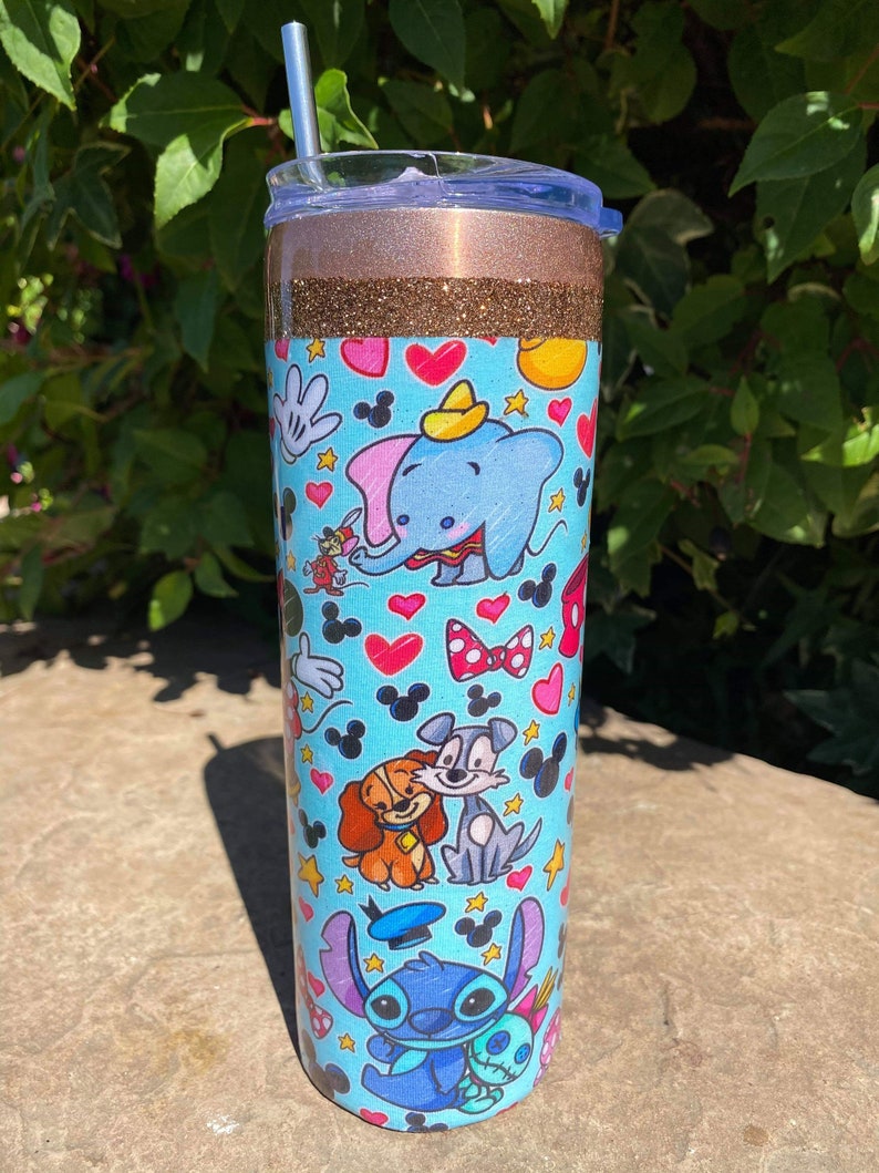 May include: A stainless steel tumbler with a blue and white design featuring various Disney characters, including Mickey Mouse, Stitch, and Lady and the Tramp. The tumbler has a gold glitter band and a clear lid.