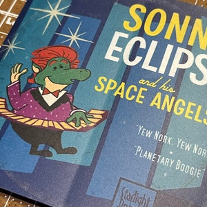 May include: A vintage 45 RPM record cover featuring a cartoon green creature with red hair playing a keyboard. The cover is blue with yellow stars and the text "SONNY ECLIPSE and his SPACE ANGELS - YEW NORK. YEW NORK 'PLANETARY BOOGIE'"