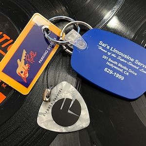 May include: A blue keychain with the text "Sal's Limousine Service" and "Home of the Super-Stretch Limos" with the address "351 South Studio Drive Hollywood, CA" and phone number "629-1999". A yellow keychain with the text "Locker Room Parking Systems" and a key graphic. A white guitar pick with a black logo that says "G-Force Records".
