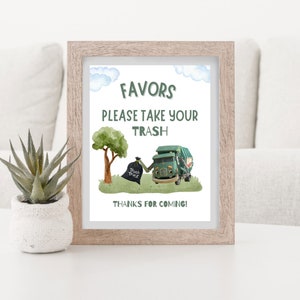 K&ouml;nnte beinhalten: Ein gerahmter Druck mit den Worten &bdquo;FAVORS PLEASE TAKE YOUR TRASH THANKS FOR COMING!&ldquo; zeigt einen Cartoon-M&uuml;llwagen, einen Baum und einen M&uuml;llsack. Der Druck befindet sich in einem hellbraunen Rahmen, mit einer kleinen Sukkulentenpflanze in einem wei&szlig;en Topf links.