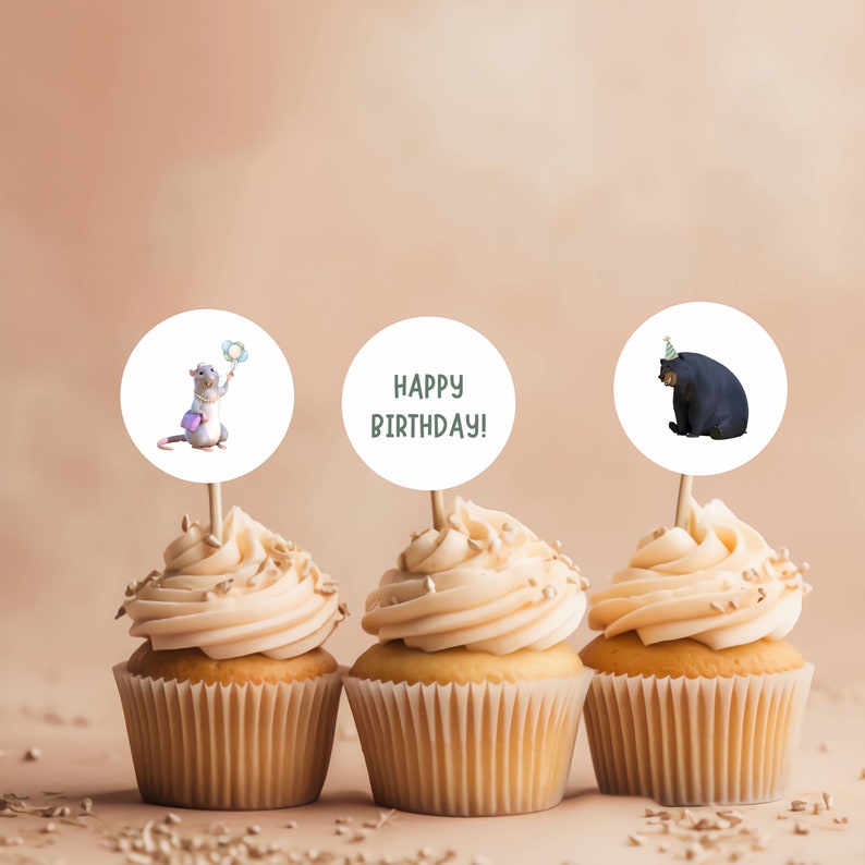 K&ouml;nnte beinhalten: Drei Cupcakes mit wei&szlig;em Frosting und Streuseln. Jeder Cupcake hat einen runden Topper mit einem anderen Design. Ein Topper zeigt eine Comic-Ratte, die einen Zauberstab h&auml;lt, ein anderer sagt "Happy Birthday!" und der letzte zeigt einen Comic-B&auml;ren, der eine Partym&uuml;tze tr&auml;gt.