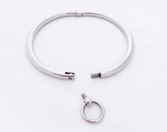May include: A silver metal choker necklace with a hinged clasp and a separate silver metal ring with a ball on the top.