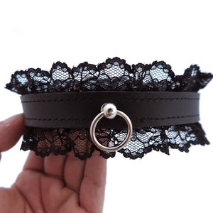 Può includere: Choker in pelle nera con un anello argentato e un bordo in pizzo nero.