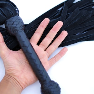 Puede incluir: Un látigo de cuero negro con un mango trenzado. El látigo mide aproximadamente 38 cm de largo y tiene una franja de tiras de cuero.