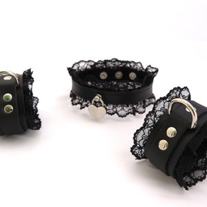May include: Three black leather and lace collars with silver hardware. Two of the collars are wrist cuffs and one is a choker with a heart-shaped pendant.