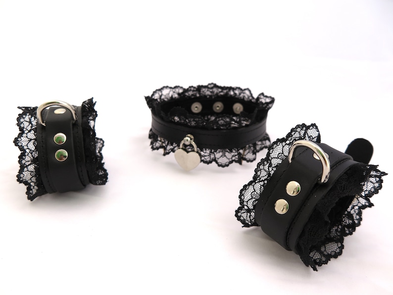 May include: Three black leather and lace collars with silver hardware. Two of the collars are wrist cuffs and one is a choker with a heart-shaped pendant.