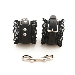 May include: A pair of black leather and lace cuffs with silver buckles and a silver connecting chain.