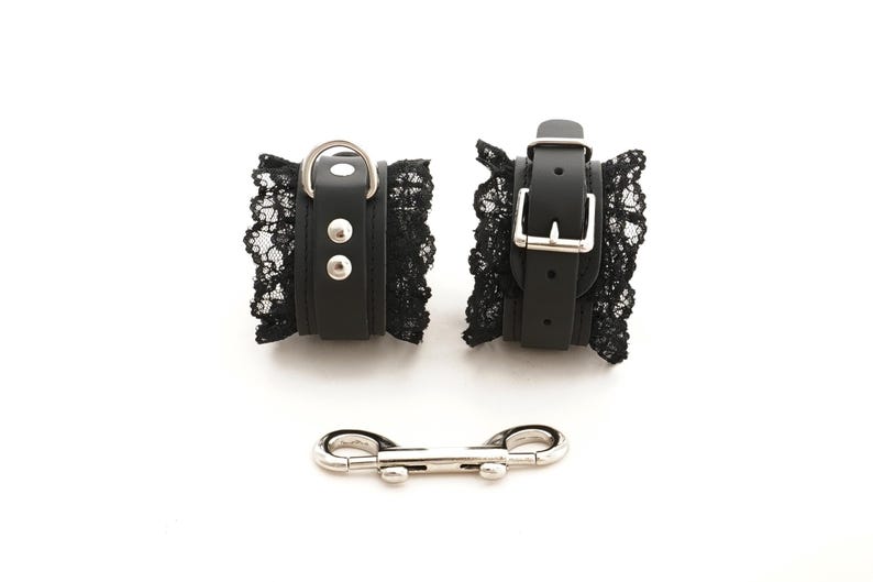 May include: A pair of black leather and lace cuffs with silver buckles and a silver connecting chain.