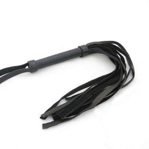 May include: A black leather whip featuring a cylindrical handle with a wrapped texture and a wrist loop at the end. The whip consists of multiple long, flat leather strips extending from the handle, creating a flexible and layered design.