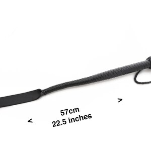 May include: Black leather riding crop with a braided handle and a flat paddle. The crop is 22.5 inches long.