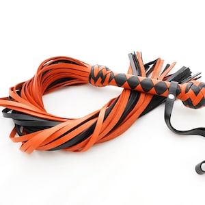 Puede incluir: Un látigo de cuero negro y naranja con un mango trenzado. El látigo está hecho de múltiples hebras de cuero que están entrelazadas.